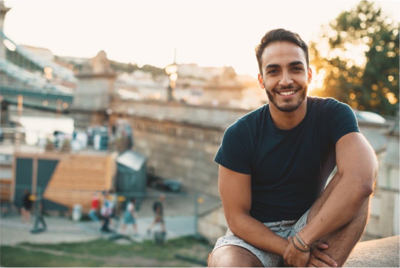 A young man smiles at golden hour above a city.
