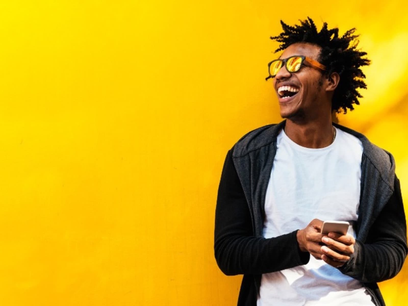 A man laughs holding his phone against a bright wall.