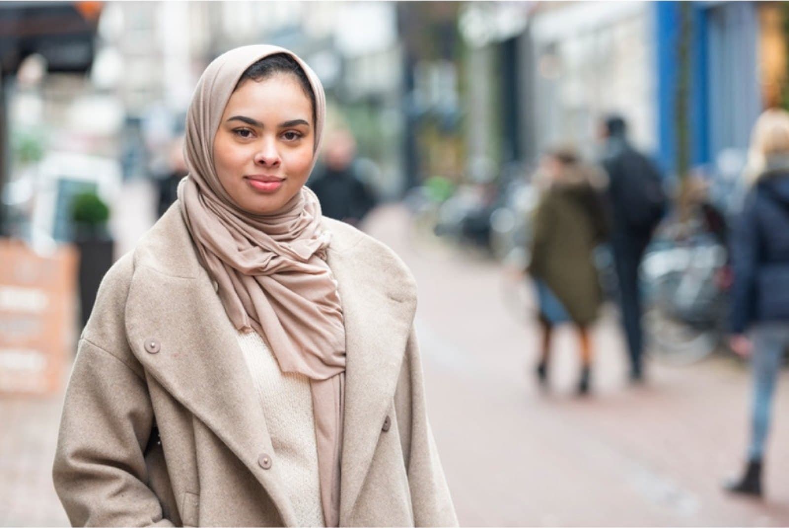 A woman in a hijab looks to the camera on a city street.